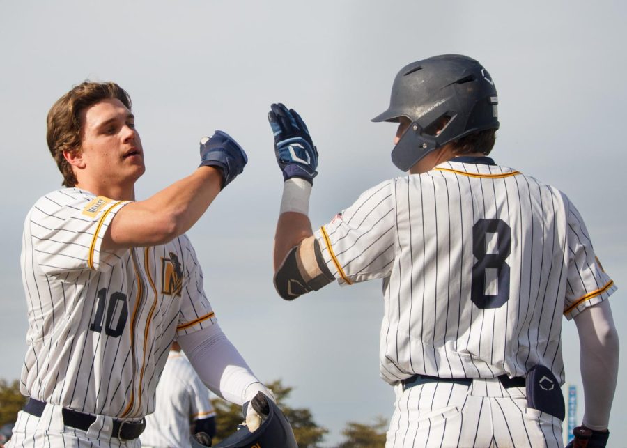 Sophomore infielder Carson Garner gives sophomre outfielder Dustin Mercer a high-five after scoring for the Racers against the Skyhawks. Photo by Rebeca Mertins Chiodini/The News.
