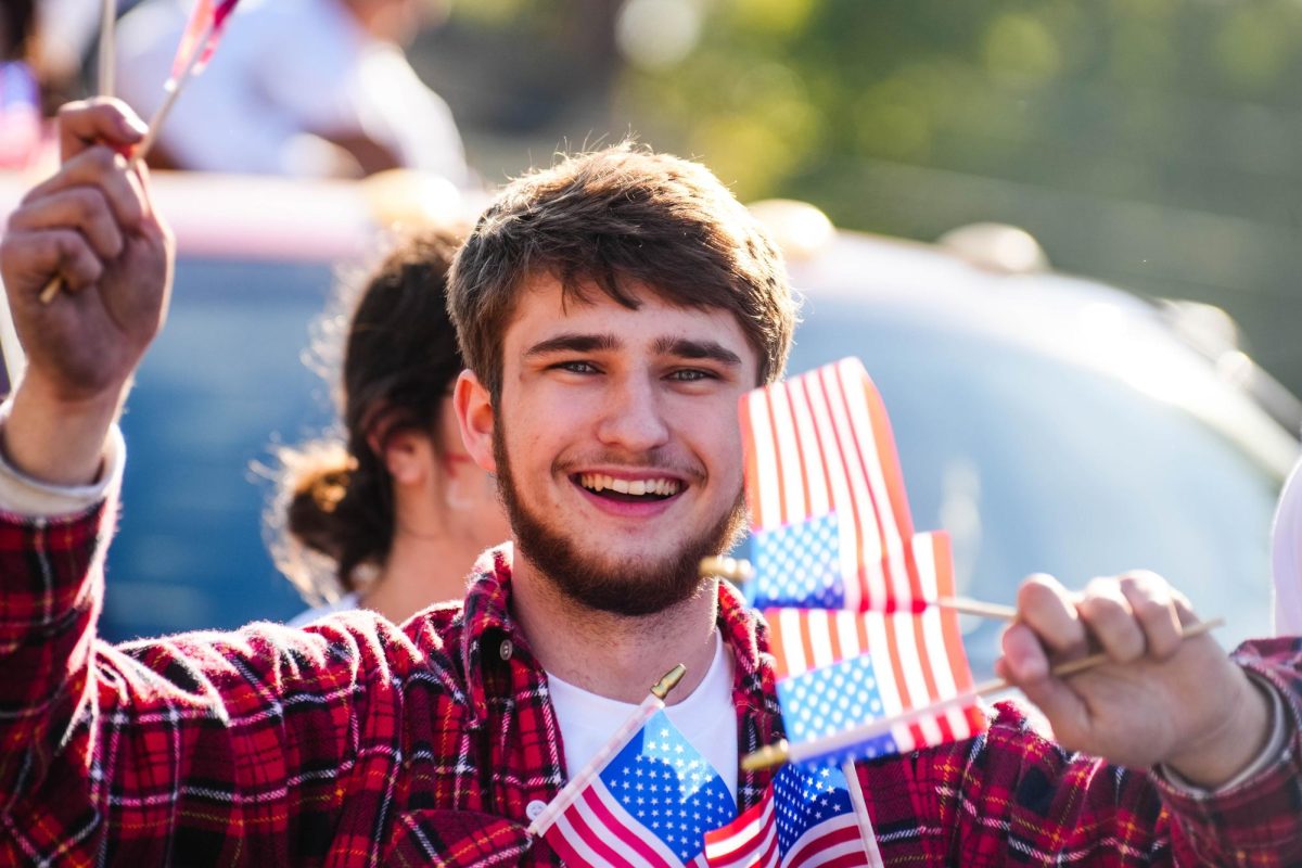 A brother of Sigma Pi smiles while holding American flags. 