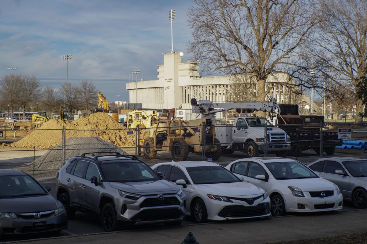 Construction vehicles, piles of dirt and gravel and equipment being used in the fenced off parking area beside Hart Hall 