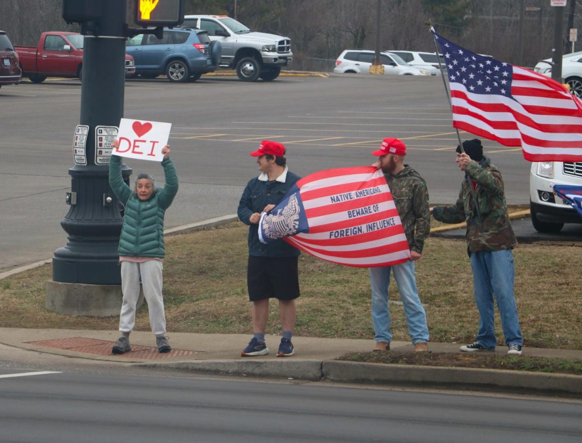 A woman with a DEI sign protests against the Trump supporters beside her.
